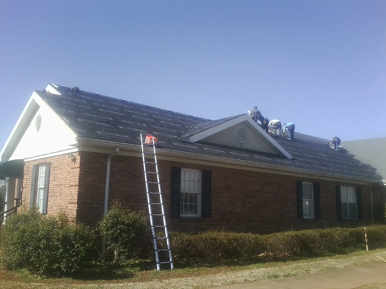 Crew tearing shingles off a brick ranch roof with a ladder set — Metal Roof Repair work by our crew in Upper Sandusky