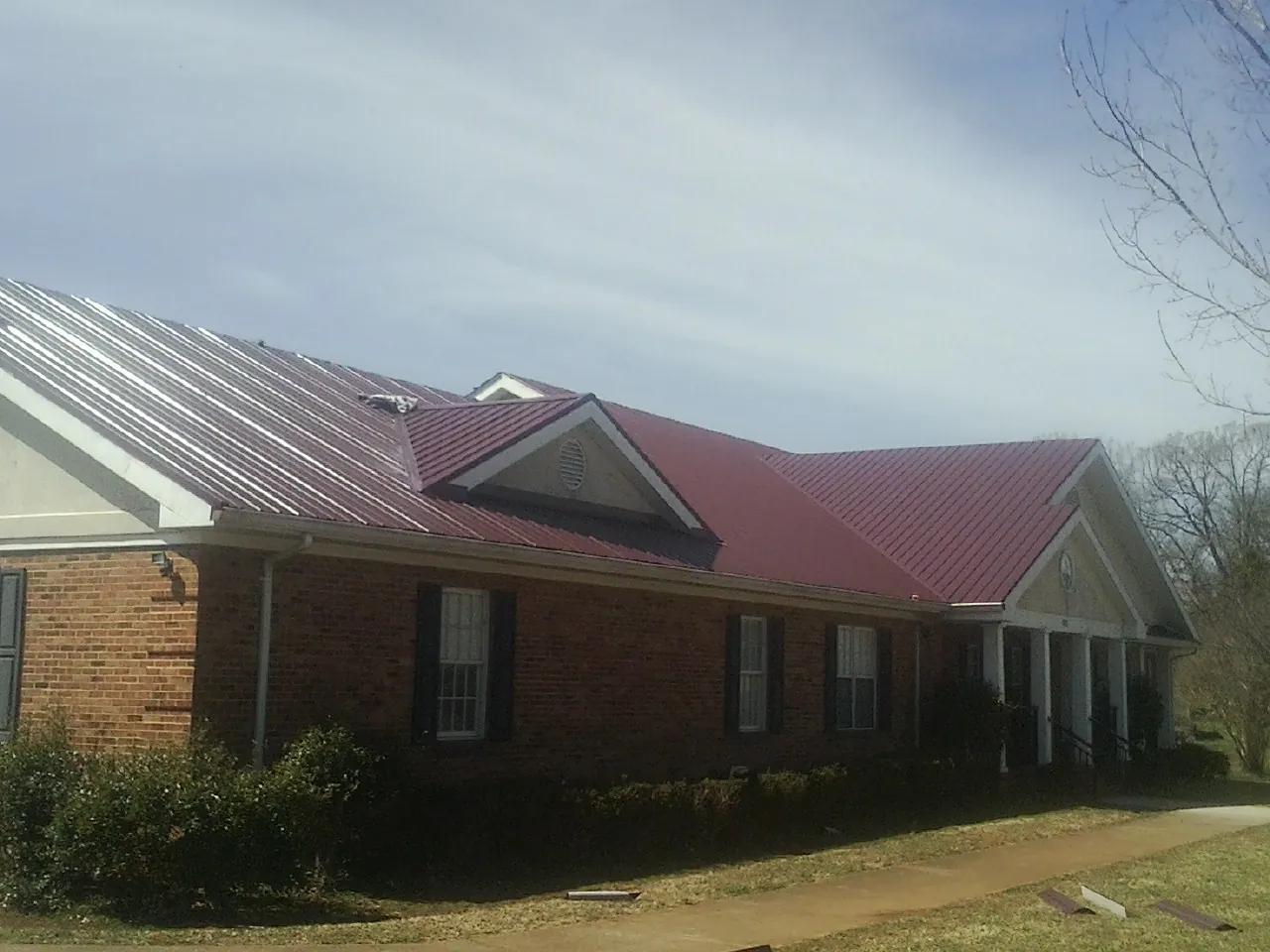 Red metal roof with gabled entries on a long brick building, from a Hail Damage Roof Repair job in Upper Sandusky