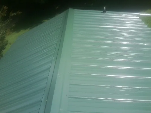 New green metal panels meeting at the ridge of a roof — Flat Roof Repair work by our crew in Upper Sandusky