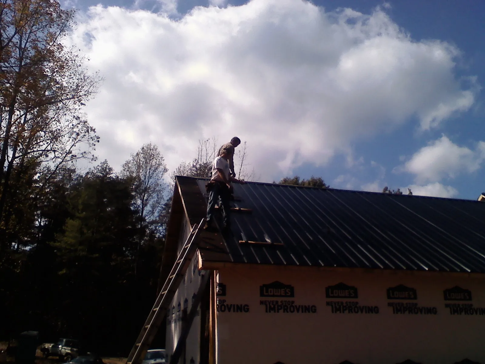Roofer fastening dark metal panels high against a cloudy sky, from a Roof Inspection job in Upper Sandusky